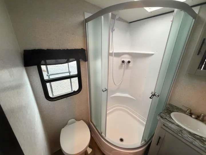 RV rental bathroom with a corner shower, toilet, and sink, showing compact design for travel comfort.. Crossroads RV Sunset Trail Super Lite 2024