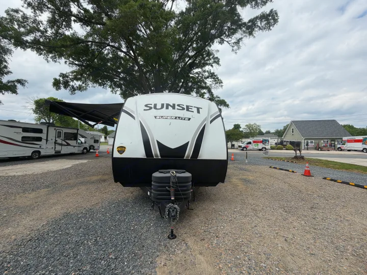 Front view of a Sunset Trail Super Lite travel trailer RV rental, parked in a gravel lot with other RVs and a U-Haul facility.. Crossroads RV Sunset Trail Super Lite 2024
