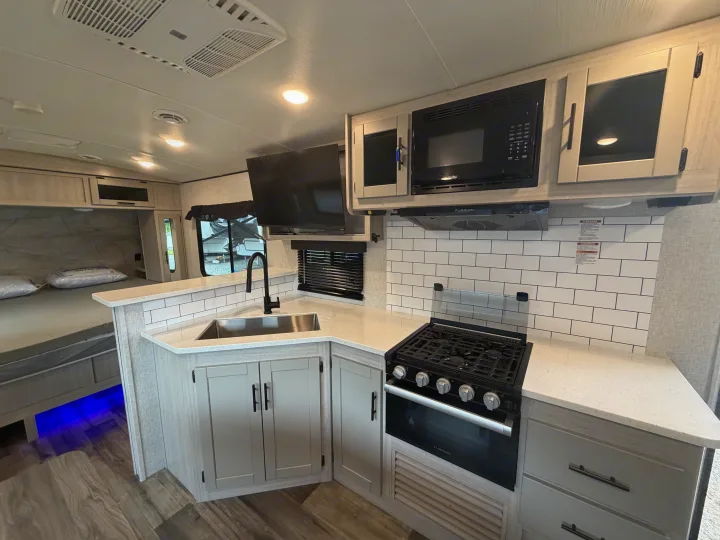 Explore this rv rental's modern kitchen with a stove, microwave, sink, and an adjacent bedroom with blue accent lighting.. Crossroads RV Sunset Trail Super Lite 2024