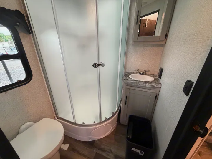 Compact RV rental bathroom showcasing a corner shower with frosted doors, a toilet, and a sink vanity with a mirror.. Crossroads RV Sunset Trail Super Lite 2024