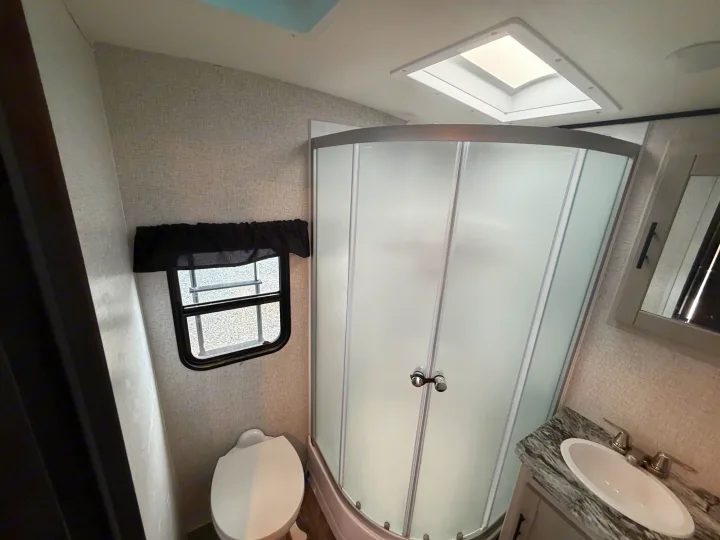 Compact RV rental bathroom featuring a toilet, curved frosted shower, vanity sink, and a ceiling skylight.. Crossroads RV Sunset Trail Super Lite 2024