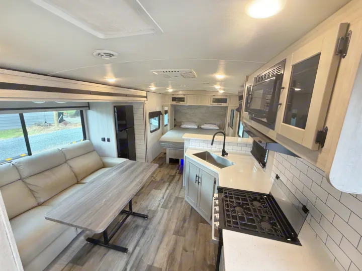 Bright and modern RV rental interior featuring a kitchen, living area with sofa, dining table, and rear bedroom.. Crossroads RV Sunset Trail Super Lite 2024