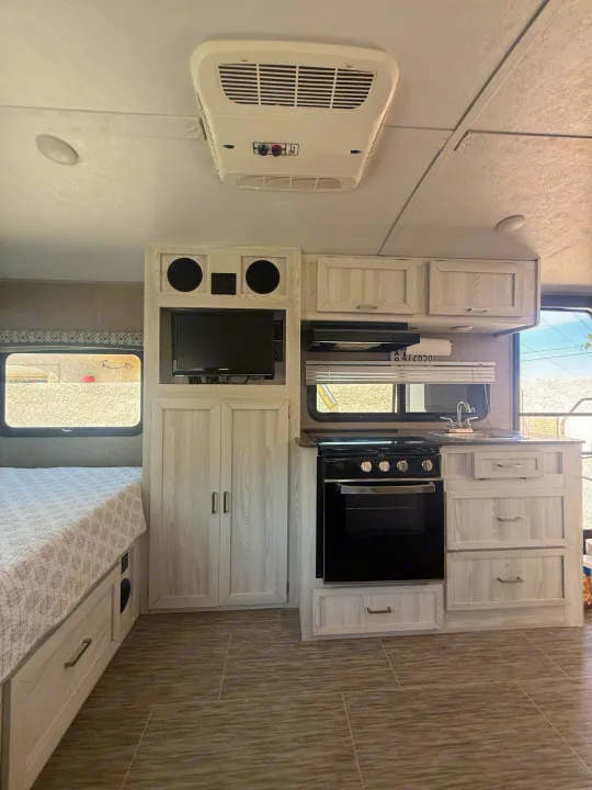 Spacious RV rental interior with a cozy bed, sleek kitchen (oven, sink), TV, and ceiling AC unit for comfort.. Forest River Flagstaff E-Pro 2018