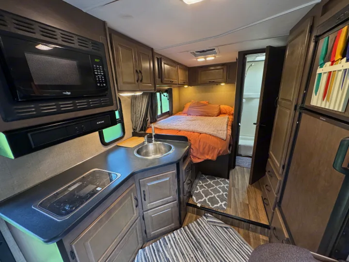 Inside a modern RV rental: a compact kitchen with microwave, stove & sink, and a comfortable bedroom with adjacent bathroom.. Thor Majestic 2018