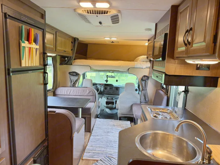 RV rental interior from rear. Features kitchen (sink, stove, microwave), dinette, overhead bunk, fridge, and front cab view.. Thor Majestic 2018