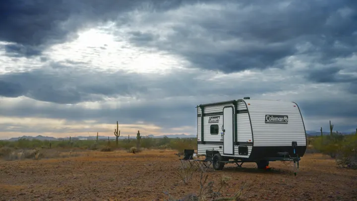 Coleman RV rental travel trailer parked for desert boondocking. Camping chairs out in a rugged landscape under a dramatic sky.. Coleman 13B 2026