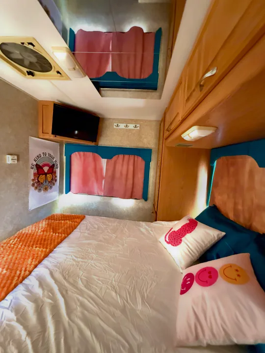 Inviting RV rental interior featuring a bed with vibrant pillows, a TV, and charming butterfly wall art in a cozy bedroom setup.. Four Winds 5000 2005
