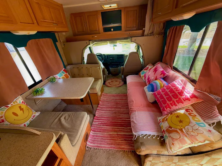 Cozy RV rental interior featuring a colorful dinette, sofa bed with smiley pillows, and a vibrant pink rug.. Four Winds 5000 2005