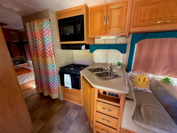 Cozy RV rental interior with a full kitchen galley, dinette, and a colorful curtain leading to the bedroom.. Four Winds 5000 2005