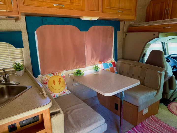 Experience this rv rental's inviting interior: a cozy dinette with cheerful pillows, compact kitchen, and practical storage for road trips.. Four Winds 5000 2005