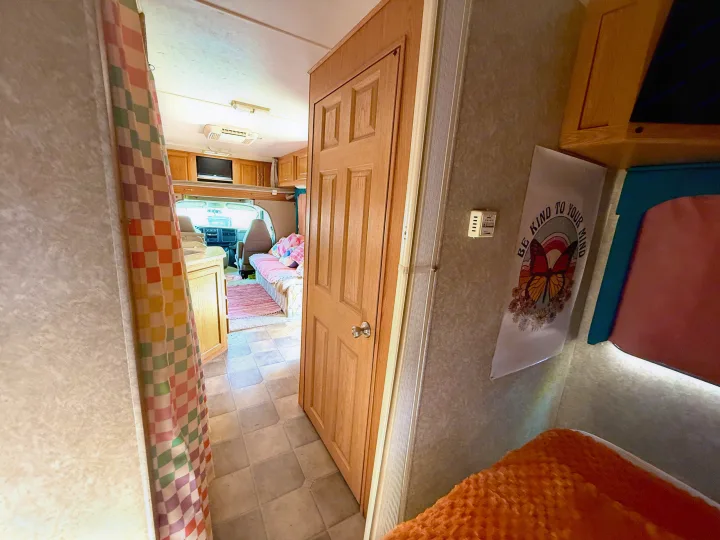 Inviting rv rental interior with front driving area, pink sofa, patterned curtain, and wooden door. "Be Kind to Your Mind" art visible.. Four Winds 5000 2005