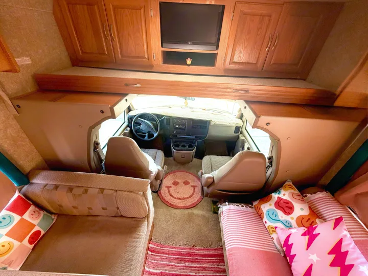 RV rental interior: living space, over-cab bunk with TV, and front cockpit. Bright, colorful decor creates a welcoming feel.. Four Winds 5000 2005