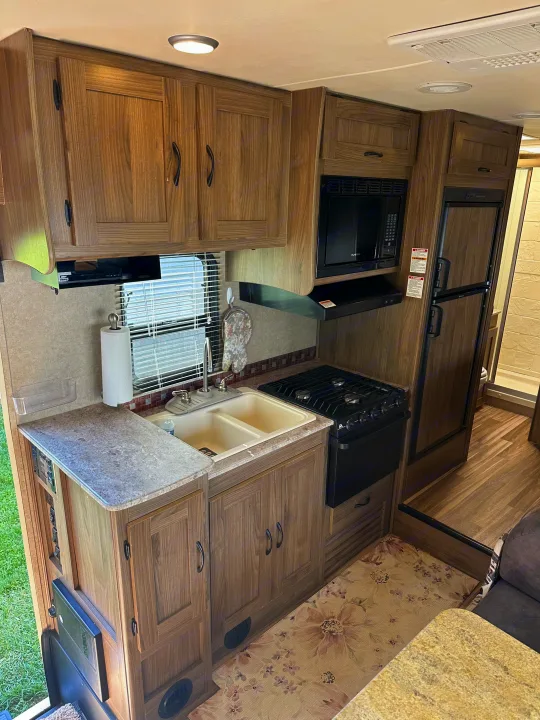 This RV rental features a compact kitchen area with wood-look cabinetry, sink, stove, microwave, and refrigerator for comfortable travel.. Coachmen Freelander 2015