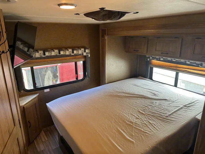 RV rental bedroom with bed, wall-mounted TV, windows, and overhead cabinets for a comfortable stay.. Coachmen Freelander 2015