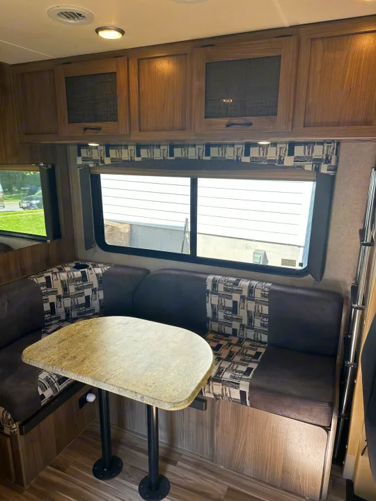 Cozy rv rental dinette featuring a table, patterned bench seating, overhead wood cabinets, and large windows.. Coachmen Freelander 2015