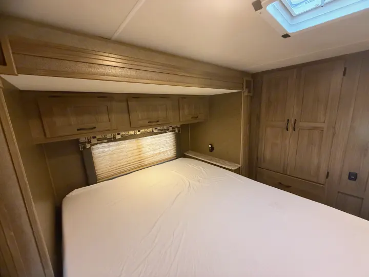 Inside an RV rental, a cozy bedroom with a white bed, wood-tone cabinets, and a wardrobe for comfortable stays.. Coachmen Freelander 2015