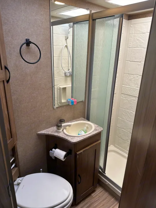 Compact RV rental bathroom: toilet, sink with soap, mirror, and enclosed shower stall.. Coachmen Freelander 2015