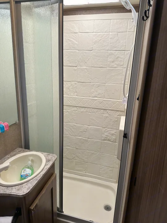 Compact RV rental bathroom: Shower with textured glass door, white patterned walls, and a small sink vanity with soap.. Coachmen Freelander 2015