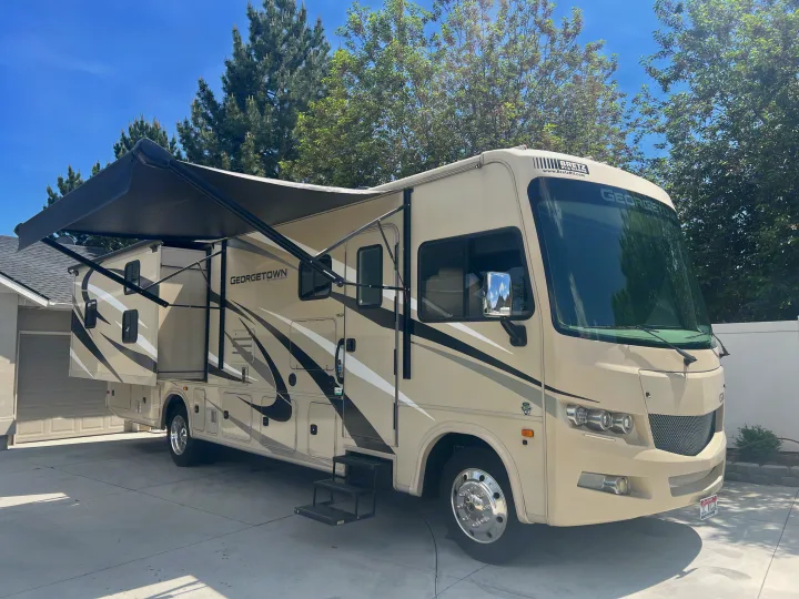 A beige Georgetown Class A RV rental with an extended awning and slide-out, parked on a sunny concrete driveway.. Georgetown GT3 2020