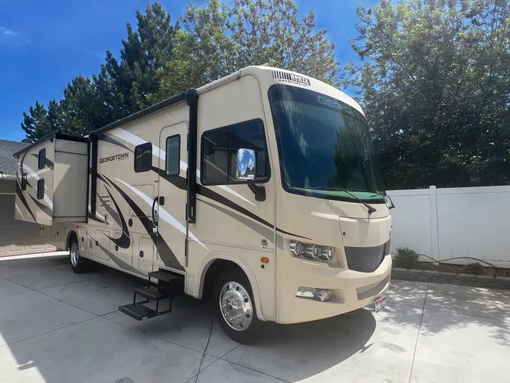 This large beige Georgetown Class A motorhome, perfect for an RV rental, is parked on a sunny driveway with its side expanded.. Georgetown GT3 2020
