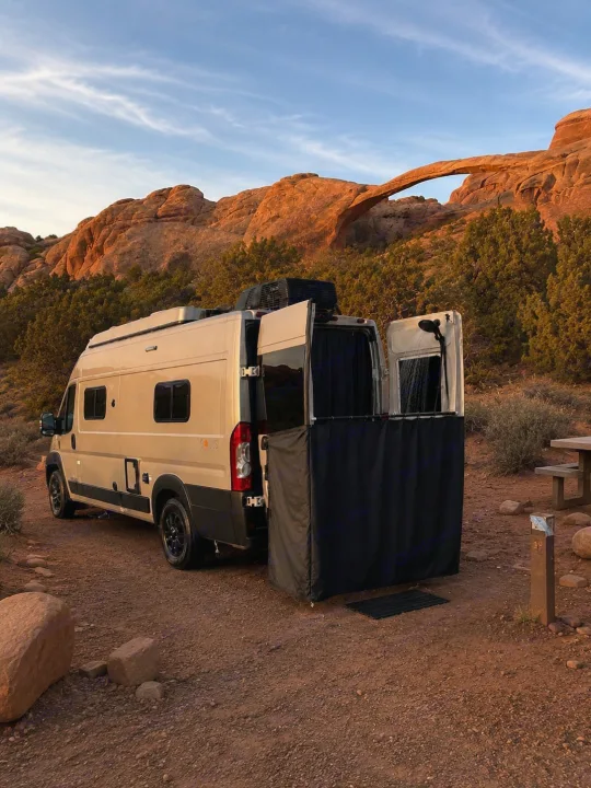 Camper van RV rental with outdoor shower setup at a desert campsite, backlit by a stunning natural arch.. Winnebago Solis 2026