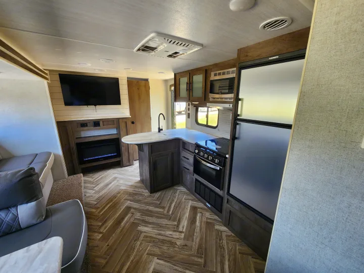 Modern **RV rental** interior showing a stylish kitchen with wood flooring and a cozy living area with TV and fireplace.. Forest River Wildwood X-Lite 2021