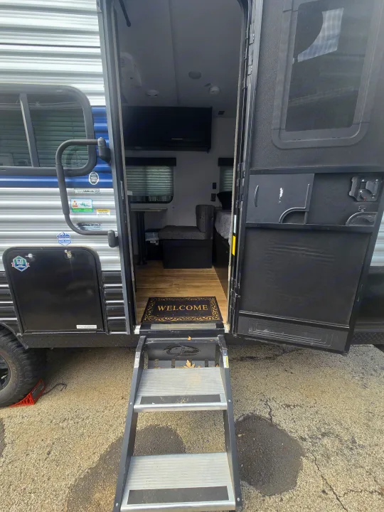 Step into this inviting RV rental! The open entrance reveals a cozy interior with a dining area, bed, and a "Welcome" mat.. Forest River Cherokee Wolf Pup 2022