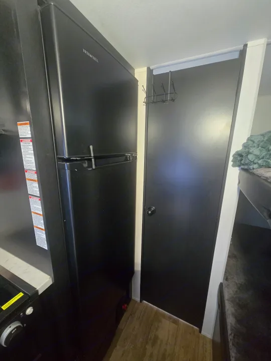 RV rental showcasing a black EVERCHILL refrigerator, door with coat rack, and bunk bed. Practical, compact living space.. Forest River Cherokee Wolf Pup 2022