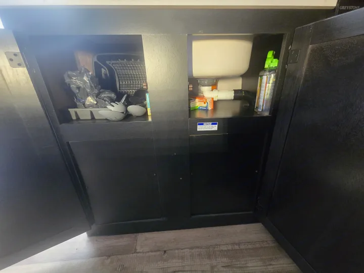 RV rental under-sink cabinet: kitchen storage, plumbing, cleaning supplies, and a notice for the waterless trap are visible.. Forest River Cherokee Wolf Pup 2022