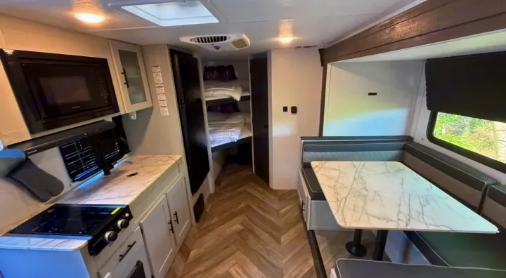 Inside this bright rv rental: a well-equipped kitchen with stove & microwave, dinette seating, and bunk beds for extra space.. Forest River Salem FSX 2022