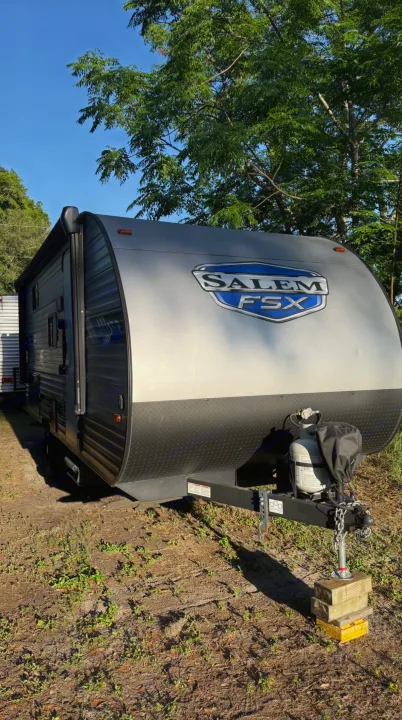This grey and black Salem FSX travel trailer is ready for your next rv rental outdoor adventure. Propane tanks visible.. Forest River Salem FSX 2022