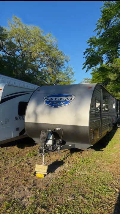 This gray 'SALEM FSX' travel trailer, perfect for an RV rental, is parked outdoors with another RV under clear blue skies and trees.. Forest River Salem FSX 2022