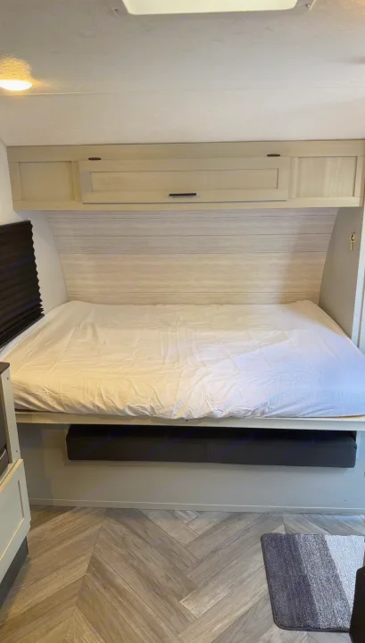 RV rental bed with white sheets, light wood cabinets above, and herringbone flooring. Compact and ready for travelers.. Forest River Salem FSX 2022