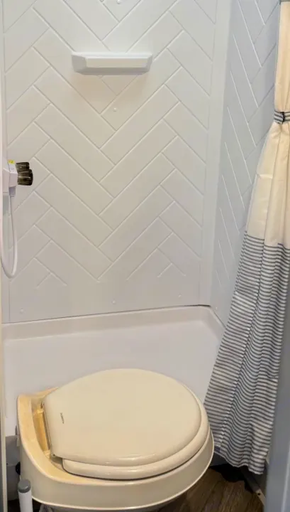 Compact RV rental bathroom with shower, white herringbone walls, and a Dometic toilet. Practical and space-saving for travel.. Forest River Salem FSX 2022