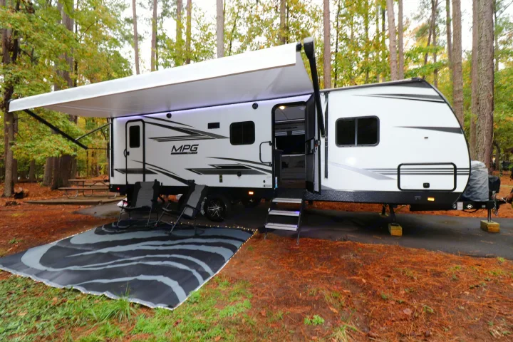 Relaxing campsite setup with an rv rental travel trailer, awning, outdoor lights, chairs, and mat in a pine forest.. Cruiser RV MPG Ultra Lite 2021