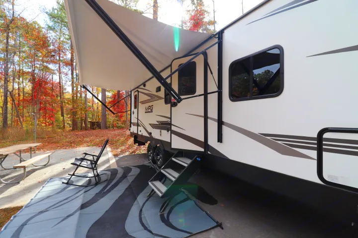 This RV rental, a travel trailer, is set up at a beautiful fall campsite with an extended awning and outdoor living space.. Cruiser RV MPG Ultra Lite 2021