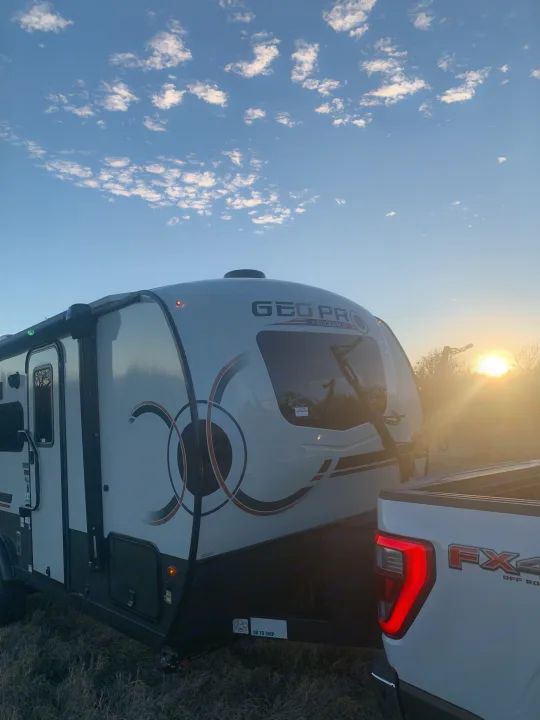 White GEO PRO RV rental trailer, with bike rack, hitched to a pickup truck at sunset under scattered clouds.. Forest River Rockwood Geo Pro 2024