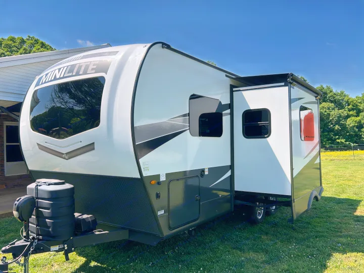 Modern white & black MiniLite travel trailer RV rental with slide-out extended, on a grassy lawn under blue sky.. Forest River Rockwood Mini Lite 2025