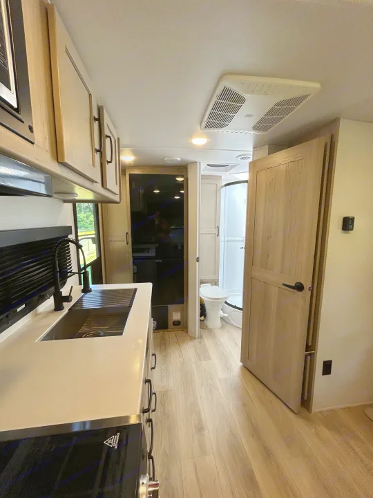 Clean rv rental interior: modern kitchen with sink, glimpse of bathroom with toilet/shower, and overhead AC unit.. Forest River Rockwood Mini Lite 2025