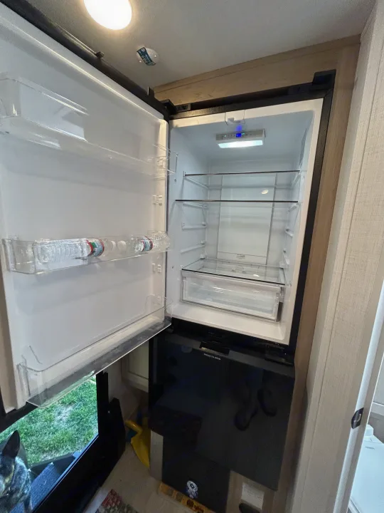 Open RV rental fridge, mostly empty, with 40°F display and "PRESS TO OPEN" on lower unit. A dog peeks below.. Forest River Rockwood Mini Lite 2025
