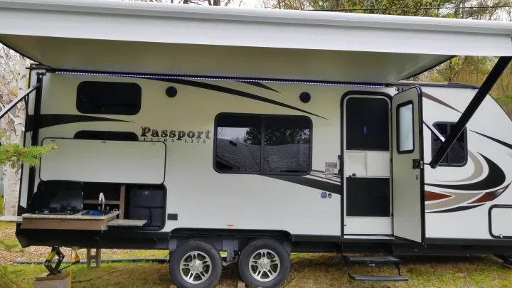 This white "Passport Ultra Lite" RV rental features an open awning with LED lights, an outdoor kitchen, and an open door.. Keystone RV Passport Ultra Lite 2019