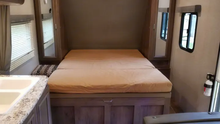 Discover this cozy rv rental bedroom, featuring a comfy bed, built-in storage, windows, and a sink area.. Keystone RV Passport Ultra Lite 2019