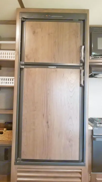 Interior of an RV rental showing a wood-paneled Dometic refrigerator with top controls, shelves & kitchen appliances.. Keystone RV Passport Ultra Lite 2019