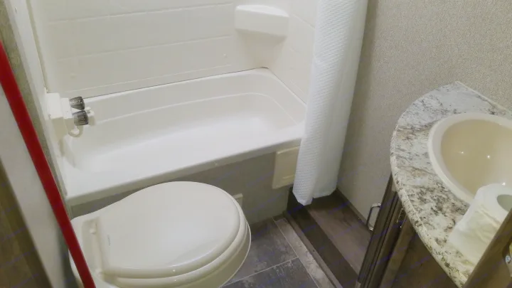 RV rental bathroom featuring a white tub/shower, toilet, and sink with a speckled countertop.. Keystone RV Passport Ultra Lite 2019