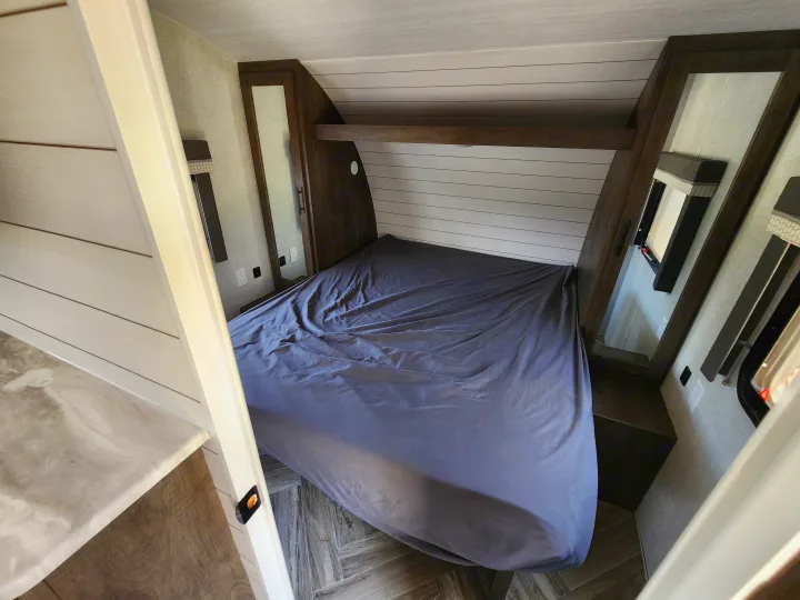 This RV rental bedroom offers a comfortable gray bed, modern wood cabinets, and a stylish white shiplap headboard.. Forest River Wildwood X-Lite 2021