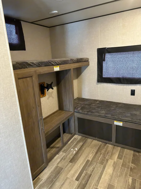 RV rental bunkhouse area: cozy bunk bed, bench seating with storage, TV mount, and window. Modern light interior walls & wood-look floor.. Crossroads RV Zinger 2021