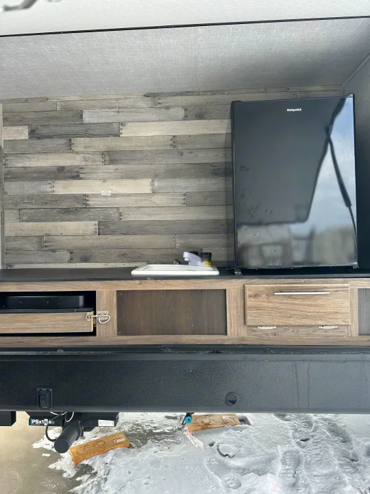 RV rental's outdoor kitchen with a Hotpoint fridge, sink, and wood-paneled backsplash, above snowy terrain.. Crossroads RV Zinger 2021
