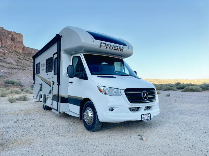 A white Prism RV rental, a Mercedes-Benz Sprinter motorhome, parked on a gravel road in a vast desert landscape.. Coachmen Prism Select 24CB 2022
