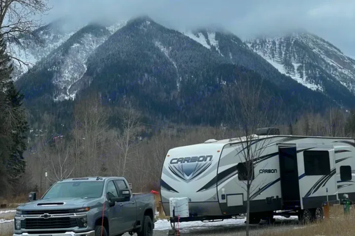 A gray pickup and Carbon RV rental travel trailer sit among snowy mountains and trees. Ideal for winter camping adventures!. Keystone Carbon 2015