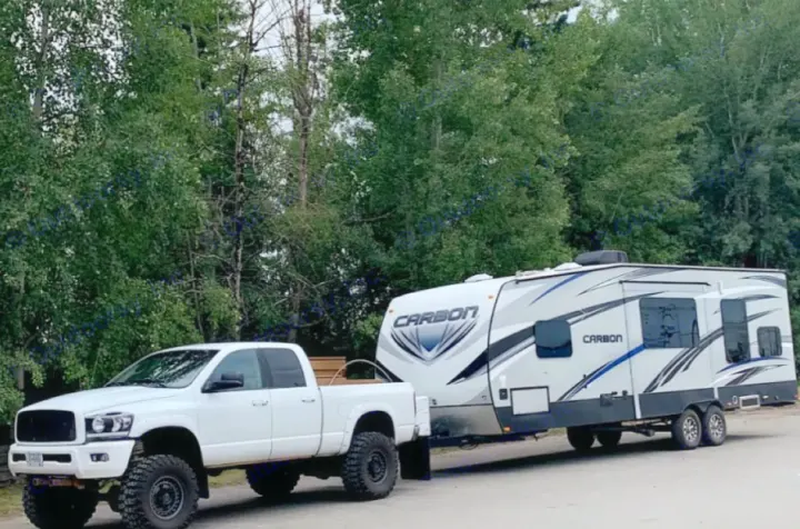 A lifted white pickup truck towing a large white and gray "CARBON" RV trailer, ready for an exciting rv rental adventure.. Keystone Carbon 2015